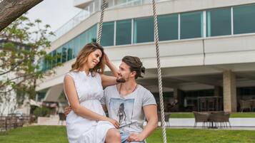 A couple sitting on a swing with a modern building in the background.