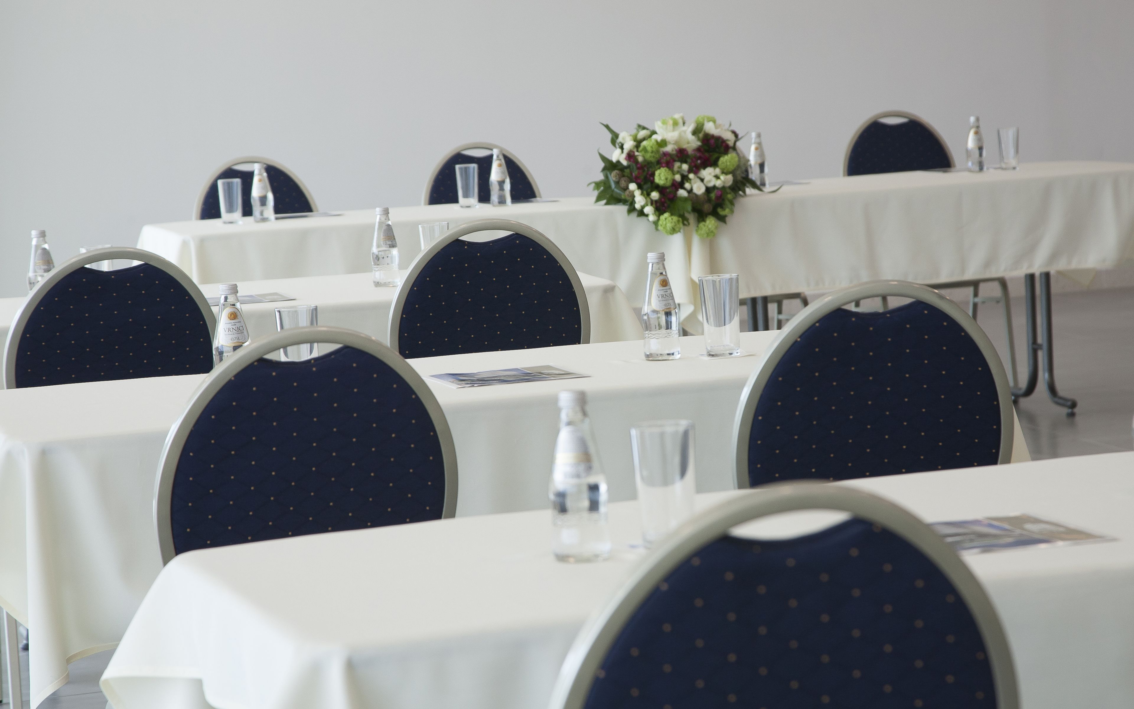A conference room with round tables, chairs, and a floral centerpiece.