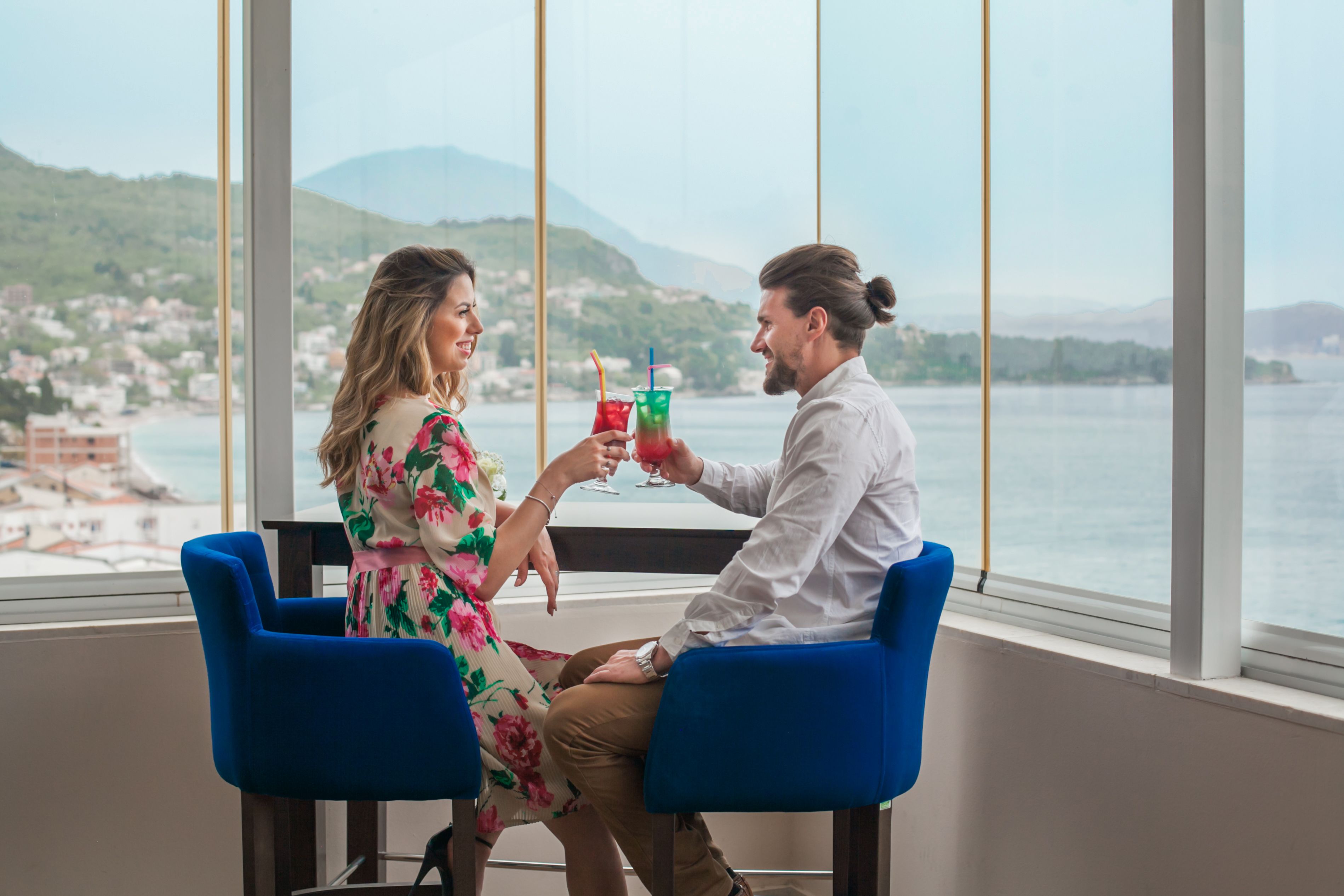 A couple seated at a table by a large window overlooking a coastal view.