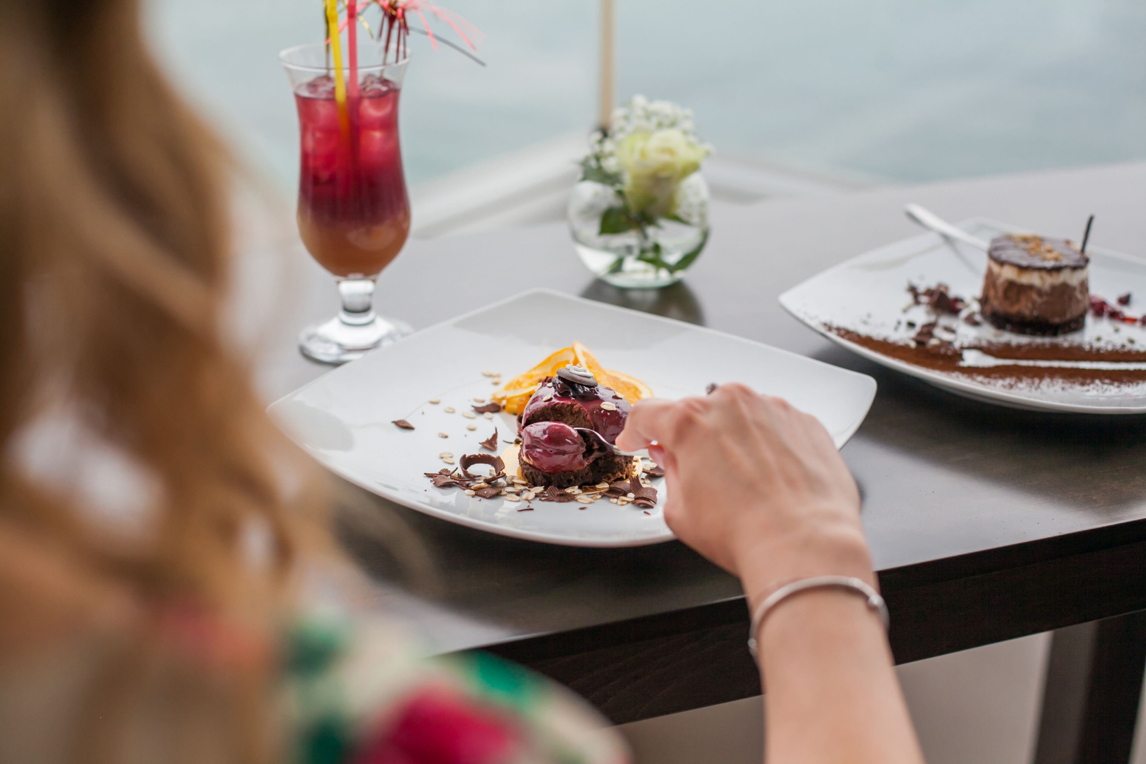 A dining table with a dessert plate, a glass of iced beverage, and a vase with flowers.