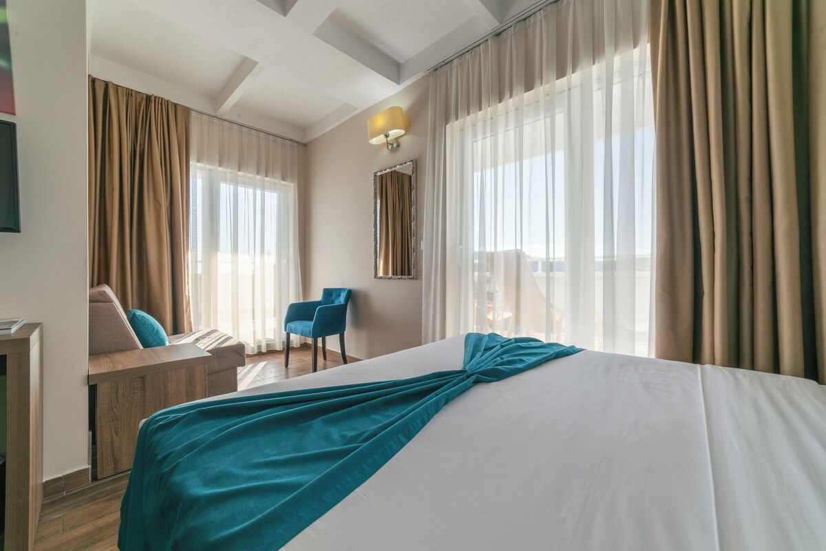 A hotel room with a bed, a desk, a chair, and a window with curtains.