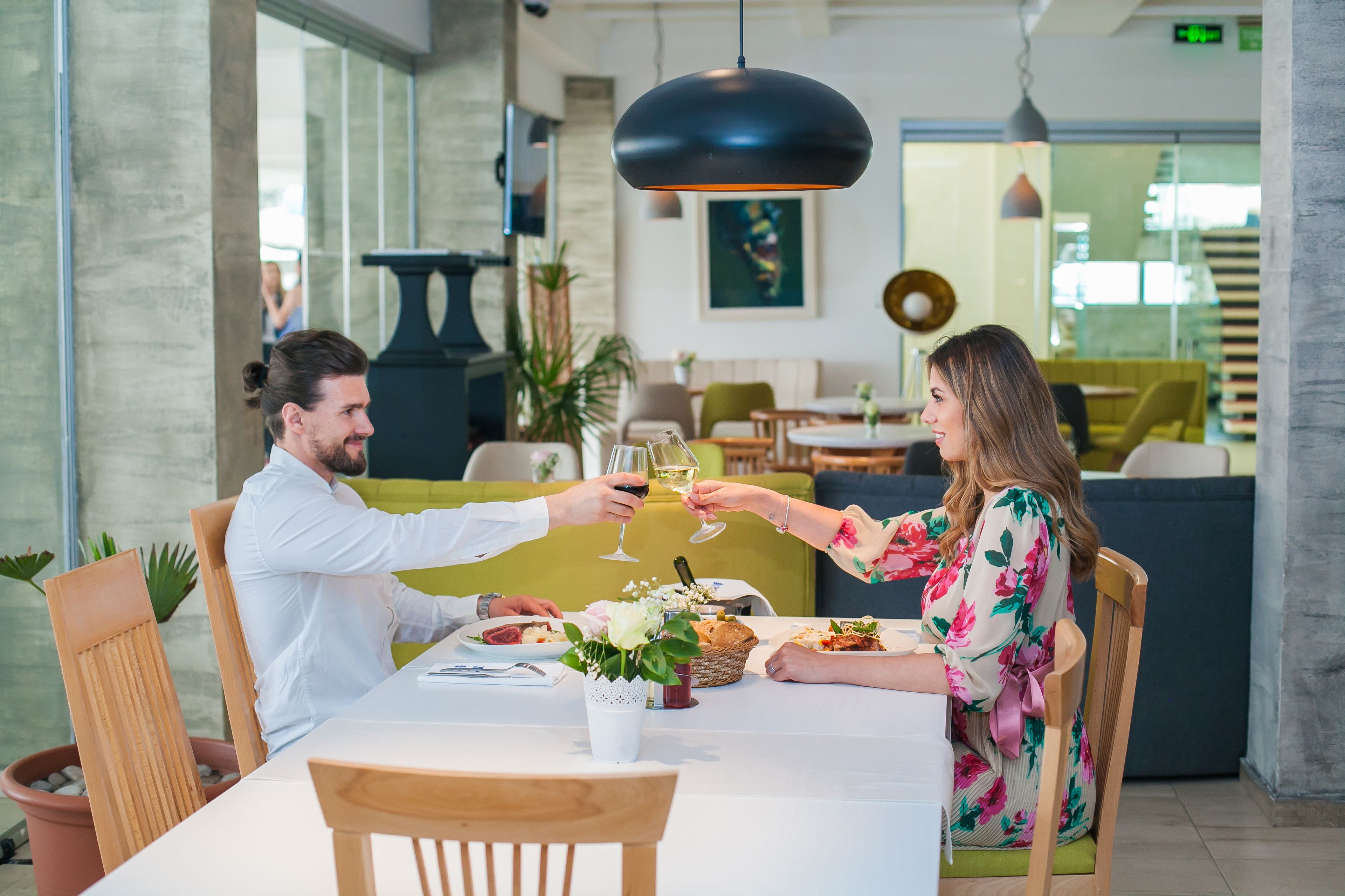 A dining area with a table set for two, a vase with flowers, and a hanging pendant light.