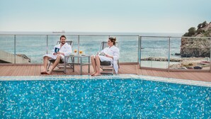 A couple relaxing by a pool with a view of the sea and a ship in the distance. - Hotel Sato (Sutomore)