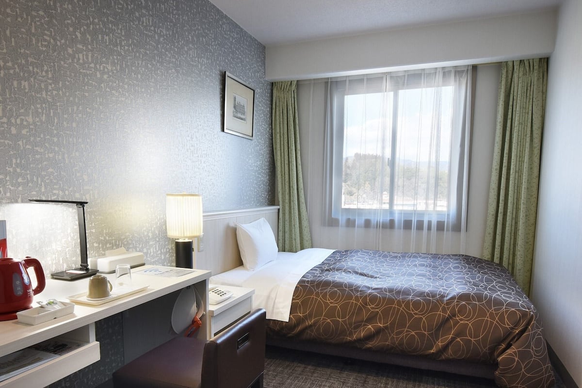 Een hotelkamer met een bed, een bureau met lamp, een telefoon en een televisie aan de wand.