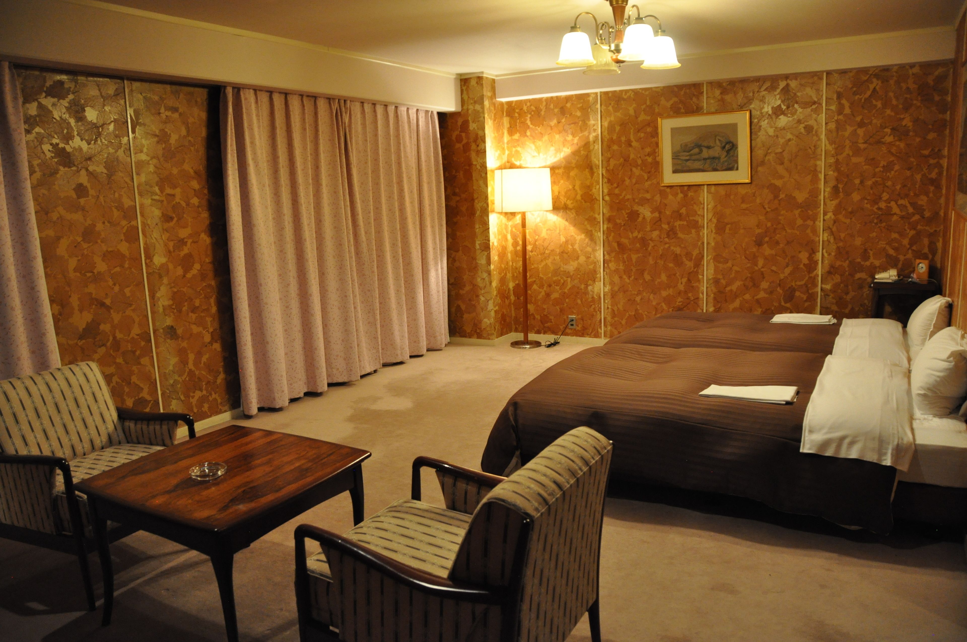 A hotel room with a large bed, two armchairs, a wooden table, and a lamp.
