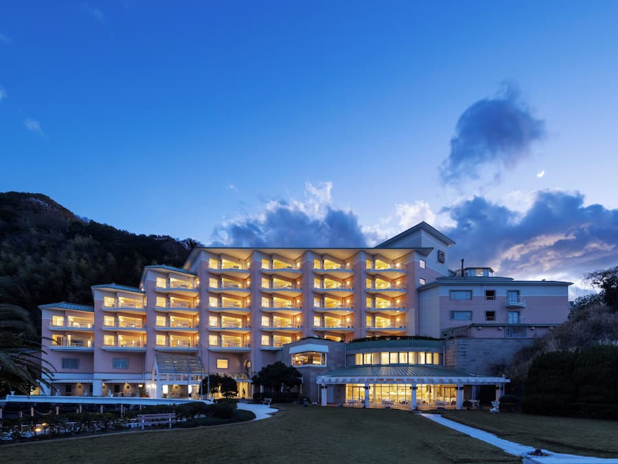 A multi-story hotel with balconies, a covered outdoor area, and a well-maintained lawn.