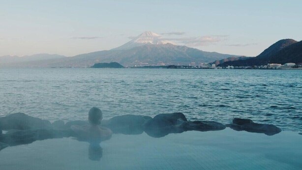 A clear view of a mountain with a snow-capped peak in the distance, a calm body of water in the foreground, and a rocky shoreline. - Awashima Hotel (Numazu)