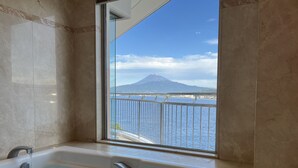 Baño con bañera y un amplio ventanal que ofrece vistas al agua y a una montaña.