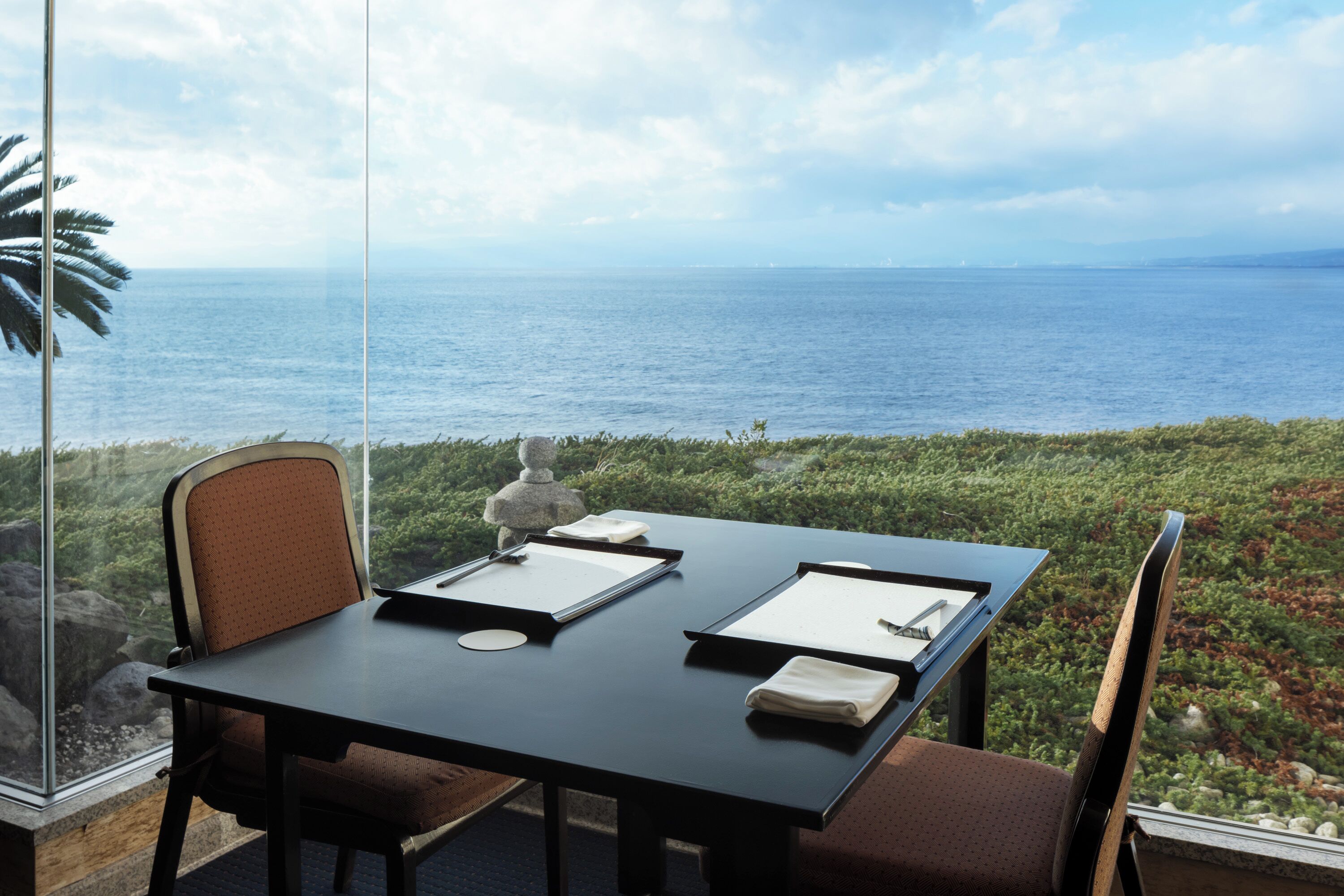 Una mesa con dos sillas, una escultura de piedra y vistas al océano.