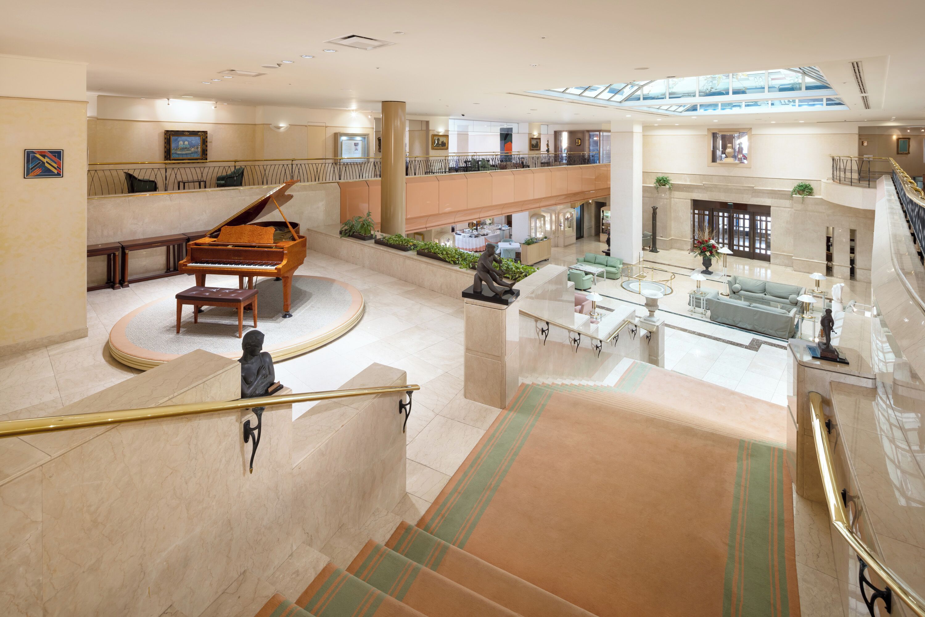 A spacious lobby with a grand piano, a statue, and a high ceiling with skylights.