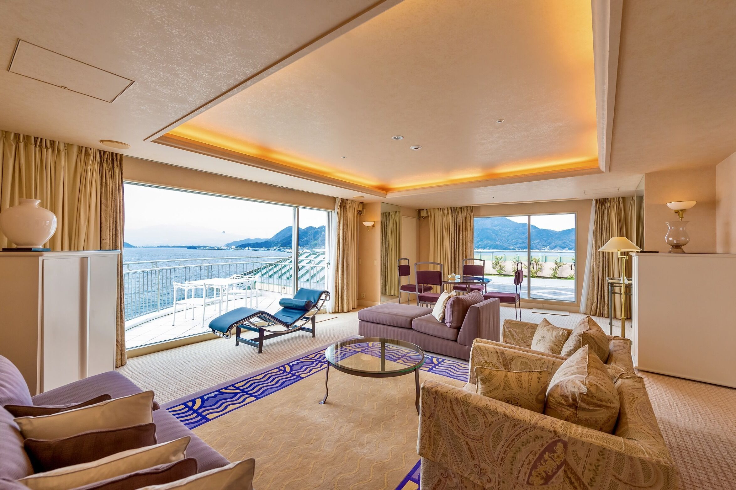 A spacious hotel room with a balcony, a sofa, a coffee table, and a dining area.