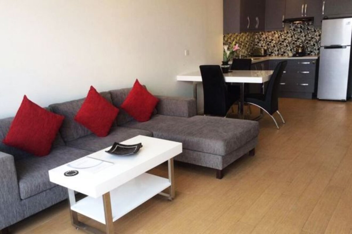 A modern living room with a grey sofa, red cushions, a white coffee table, and a dining area with a white table and black chairs.