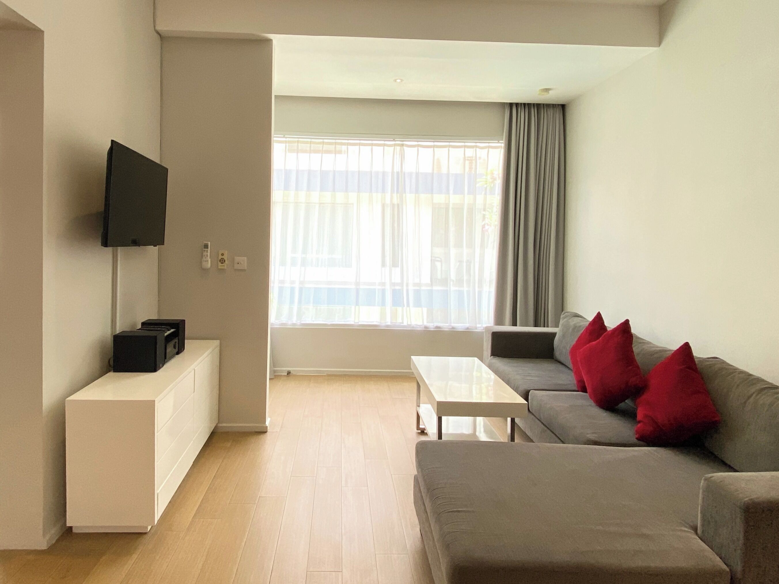 A modern living room with a grey sofa, a white coffee table, and a flat-screen TV mounted on the wall.