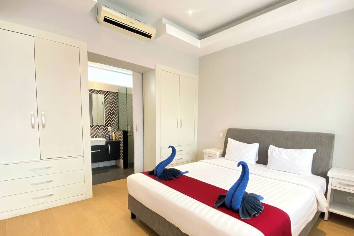 Une chambre d’hôtel avec un grand lit, une armoire blanche et une salle de bain équipée d’un miroir et d’un lavabo.