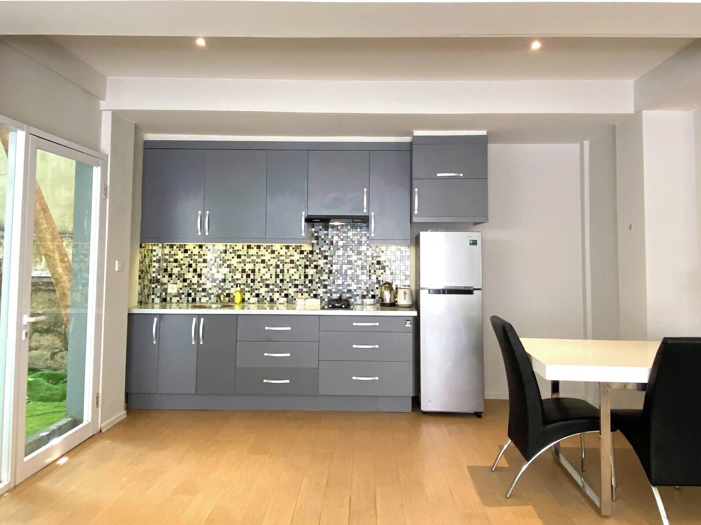A modern kitchen with grey cabinets, a stainless steel refrigerator, and a tiled backsplash.