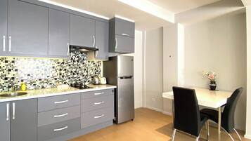 A modern kitchen with grey cabinets, a tiled backsplash, a stainless steel refrigerator, and a dining area with a white table and black chairs.