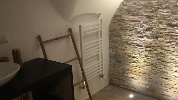 A room with a stone wall, a white radiator, and a wooden ladder leaning against the wall. There is a black table with a white bowl on it and wooden storage boxes labeled with numbers. - B&B Torino Très Chic (Turin)