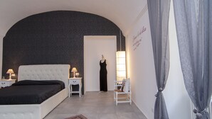 A bedroom with a white bed, a nightstand with a lamp, a chair, and a mannequin dressed in black. - B&B Torino Très Chic (Turin)