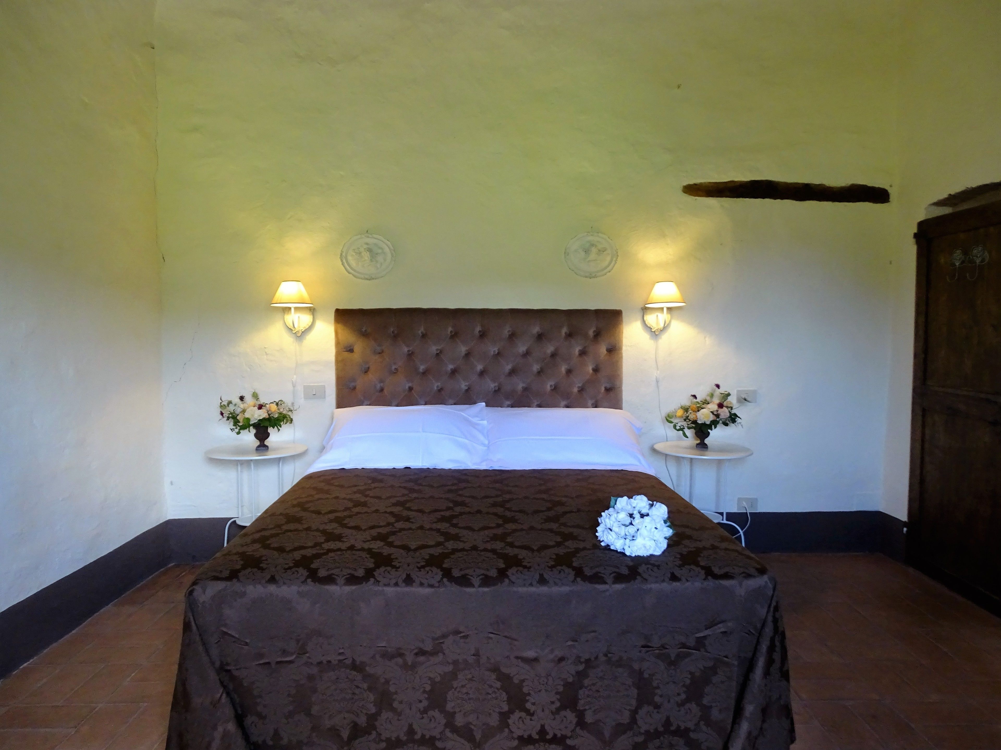 A bedroom with a tufted headboard, two bedside tables with lamps, and a floral arrangement on each table.