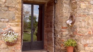 A stone building entrance with a wooden door, a stone archway, and a potted plant on the right. - Podere Pievina Delle Corti (Sinalunga)