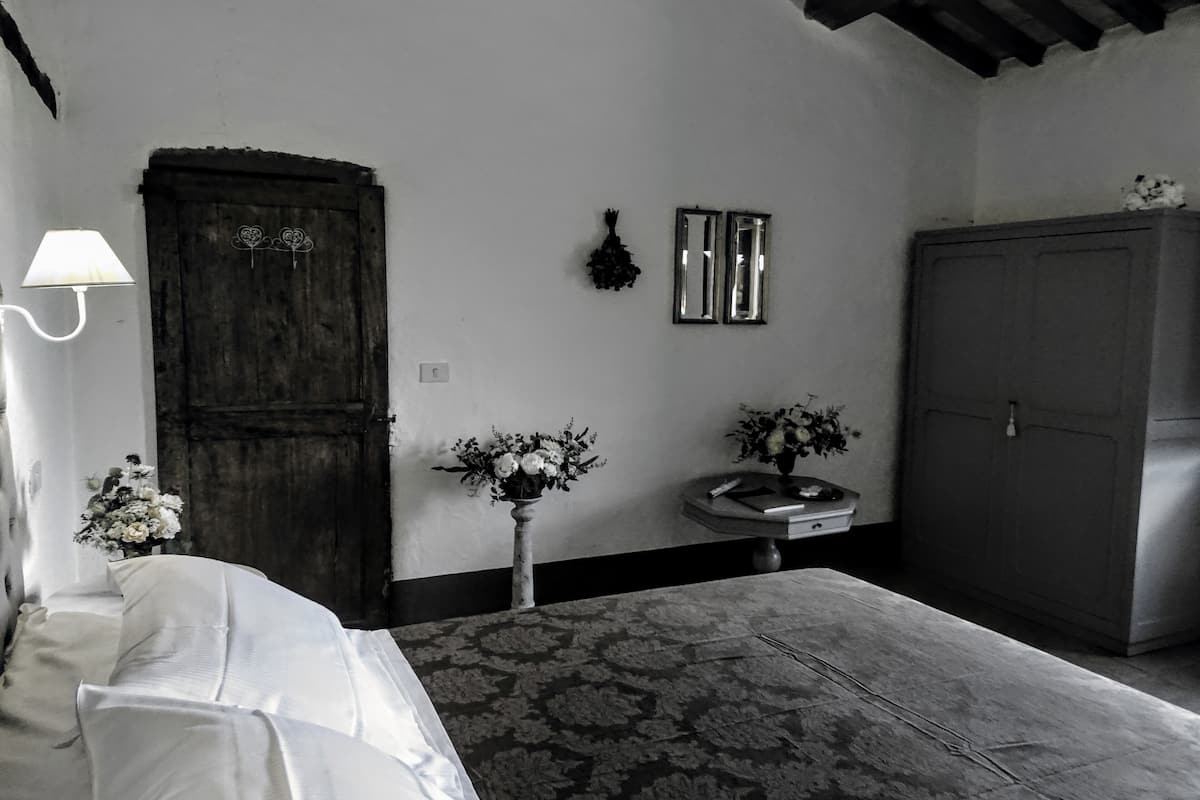 A bedroom with a bed, a dresser, a nightstand, a lamp, and two wall-mounted mirrors.