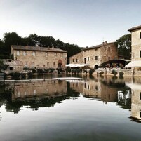 Un edificio histórico de piedra con un patio interior y un pequeño puente sobre una superficie acuática tranquila.