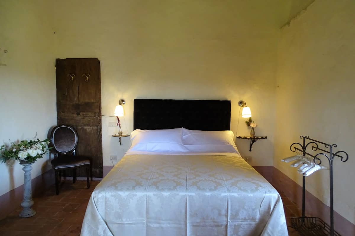 A neatly made bed with a headboard, two wall-mounted lamps, a chair, and a small table with a vase of flowers.