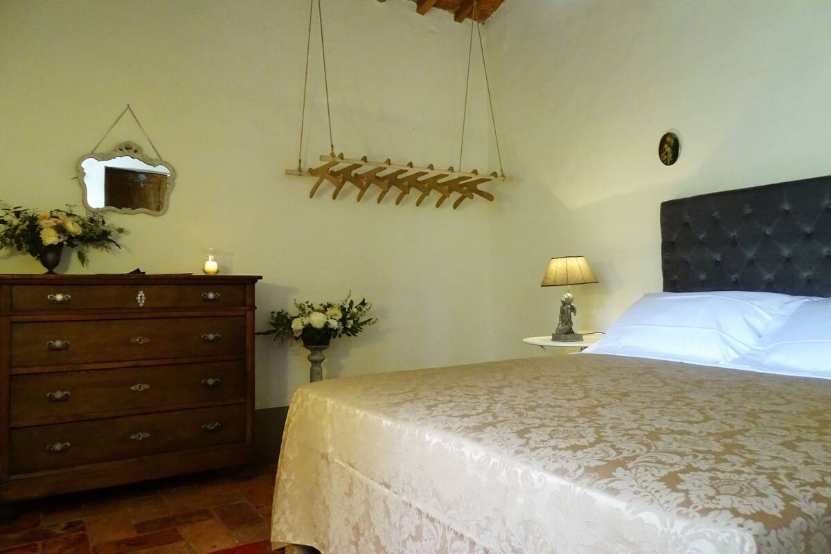 A bedroom with a bed, a dresser, a nightstand, a lamp, and a wall-mounted mirror.