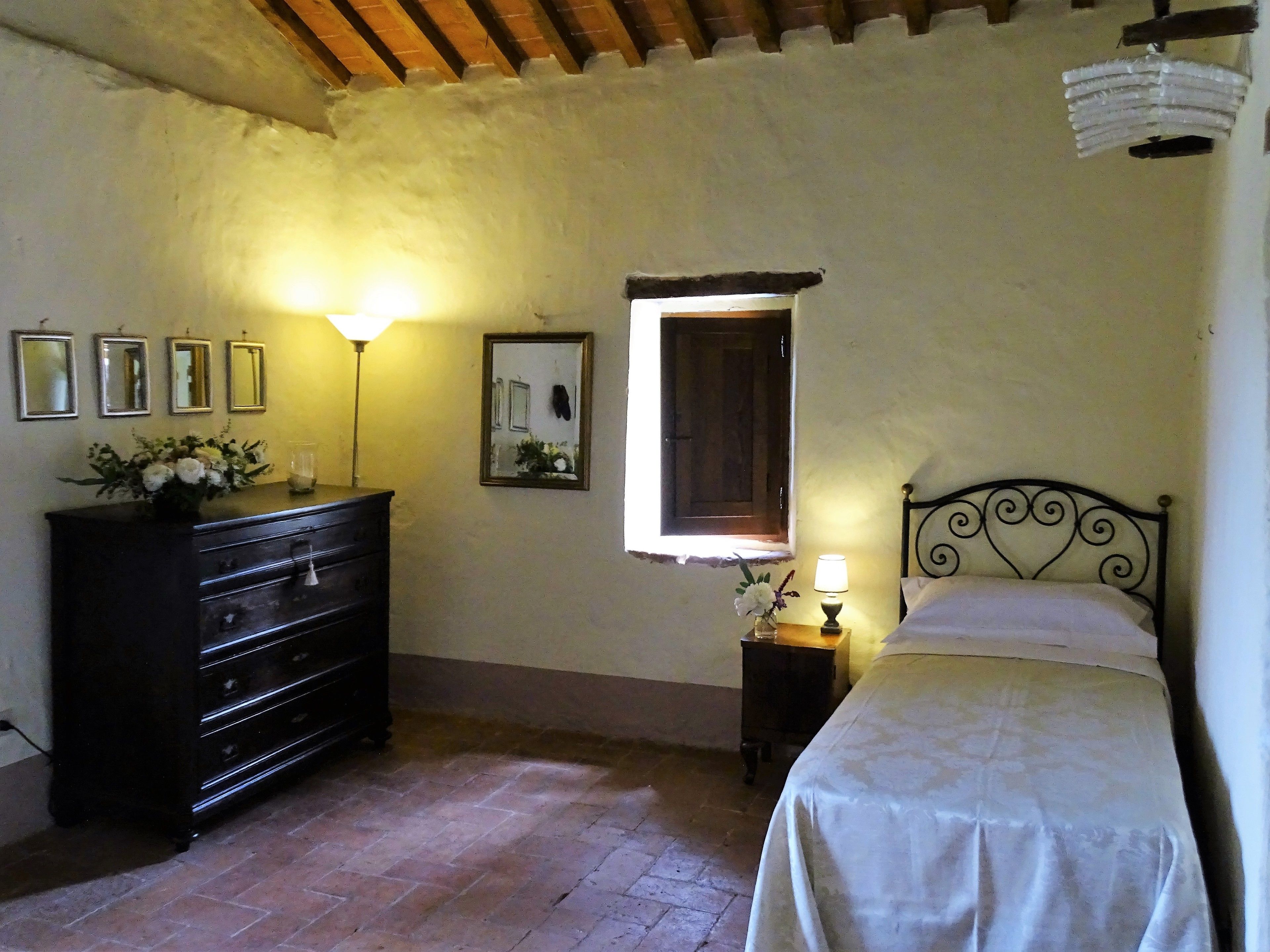A bedroom with a bed, dresser, lamp, and a window.