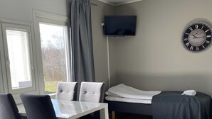 Una habitación con cama, televisión instalada en la pared, un reloj y un rincón comedor con sillas y una mesa.