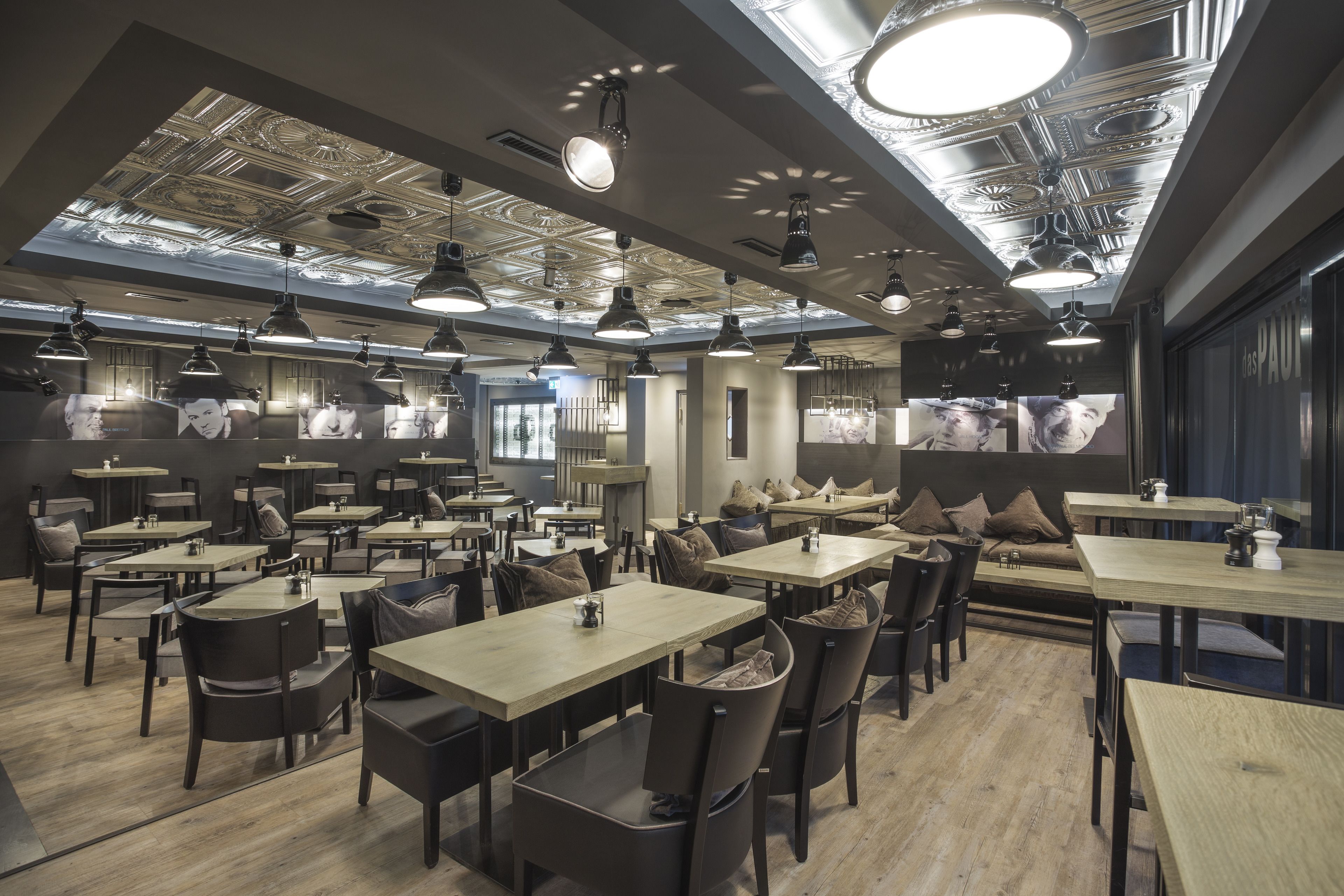 A modern restaurant with multiple dining areas, pendant lighting, and a ceiling with intricate designs.