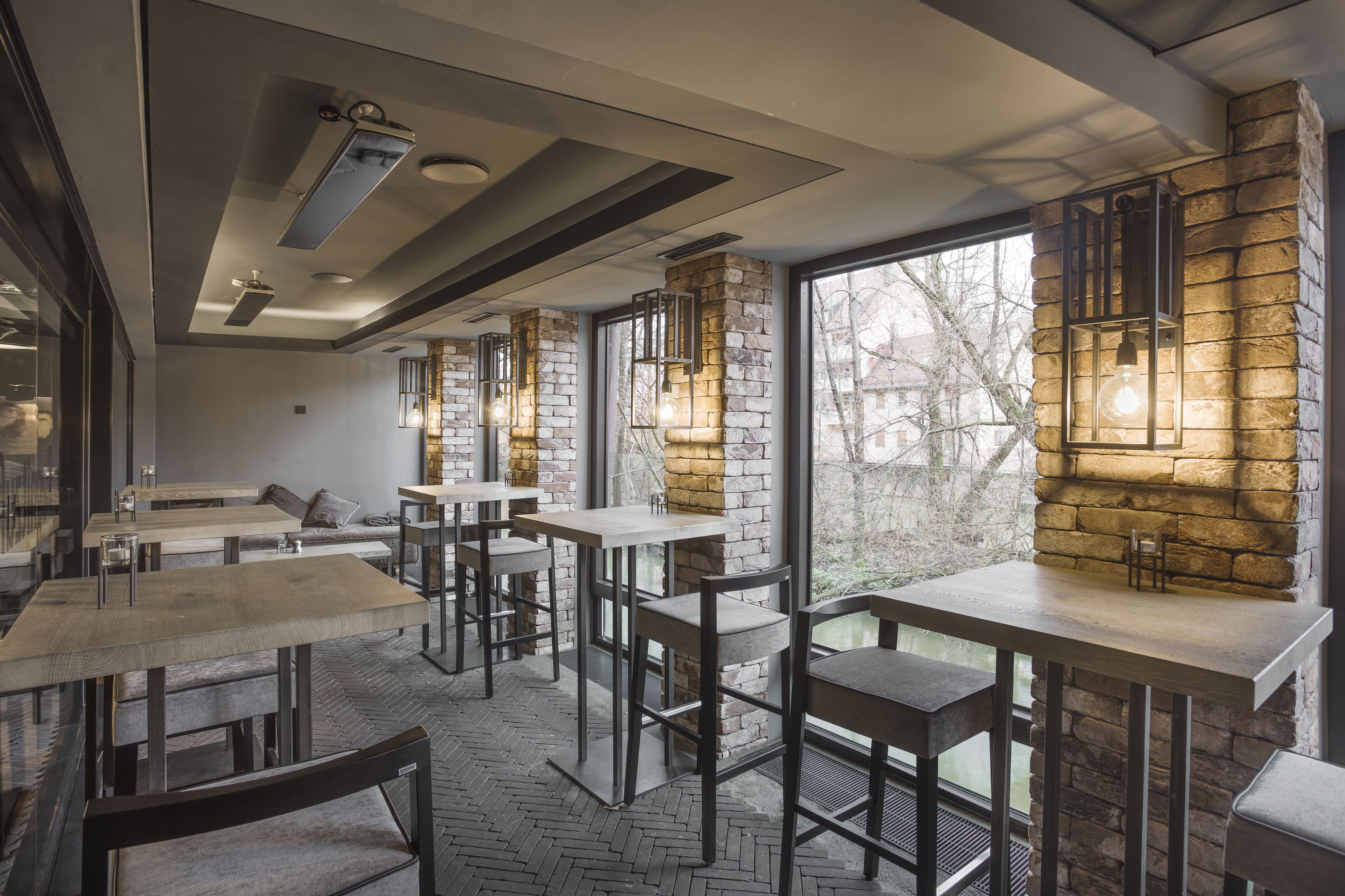 A modern restaurant interior with stone walls, wooden tables, and hanging light fixtures.
