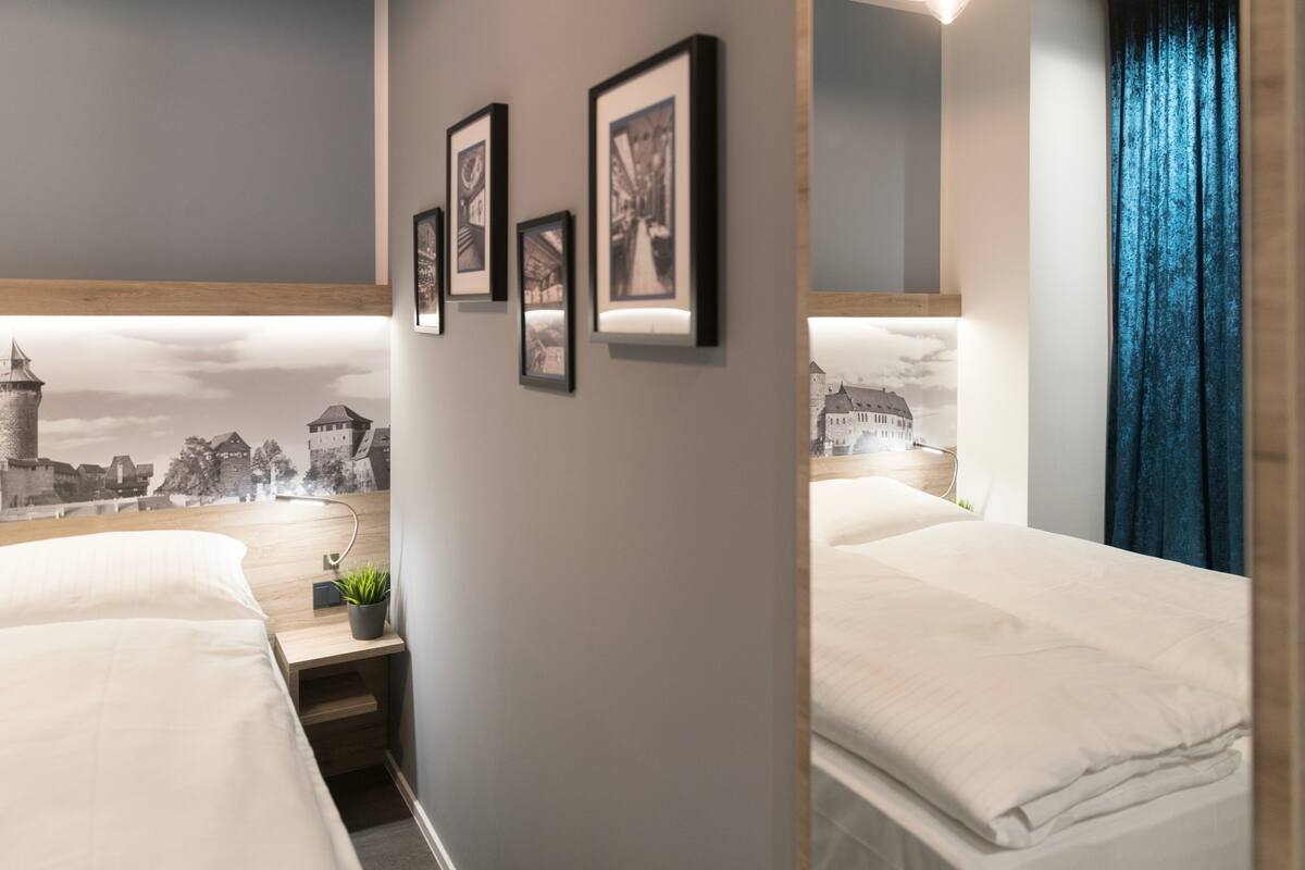 Habitación de hotel con dos camas, un escritorio en la pared, una planta pequeña y cuadros enmarcados.