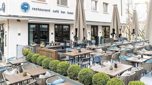 An outdoor café area with multiple tables and chairs, umbrellas, and a building with a sign indicating it is a restaurant, café, bar, and hotel. - dasPaul Hotel (Nuremberg)