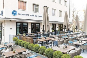 Un área de café al aire libre con varias mesas y sillas, sombrillas y un edificio con un letrero que indica que es restaurante, café, bar y hotel.