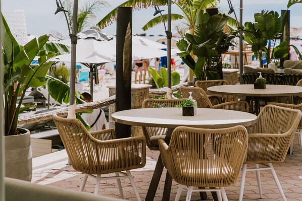 An outdoor seating area with wicker chairs and tables, surrounded by tropical plants and umbrellas. - Margarita Sea Side Hotel (Kassandra)