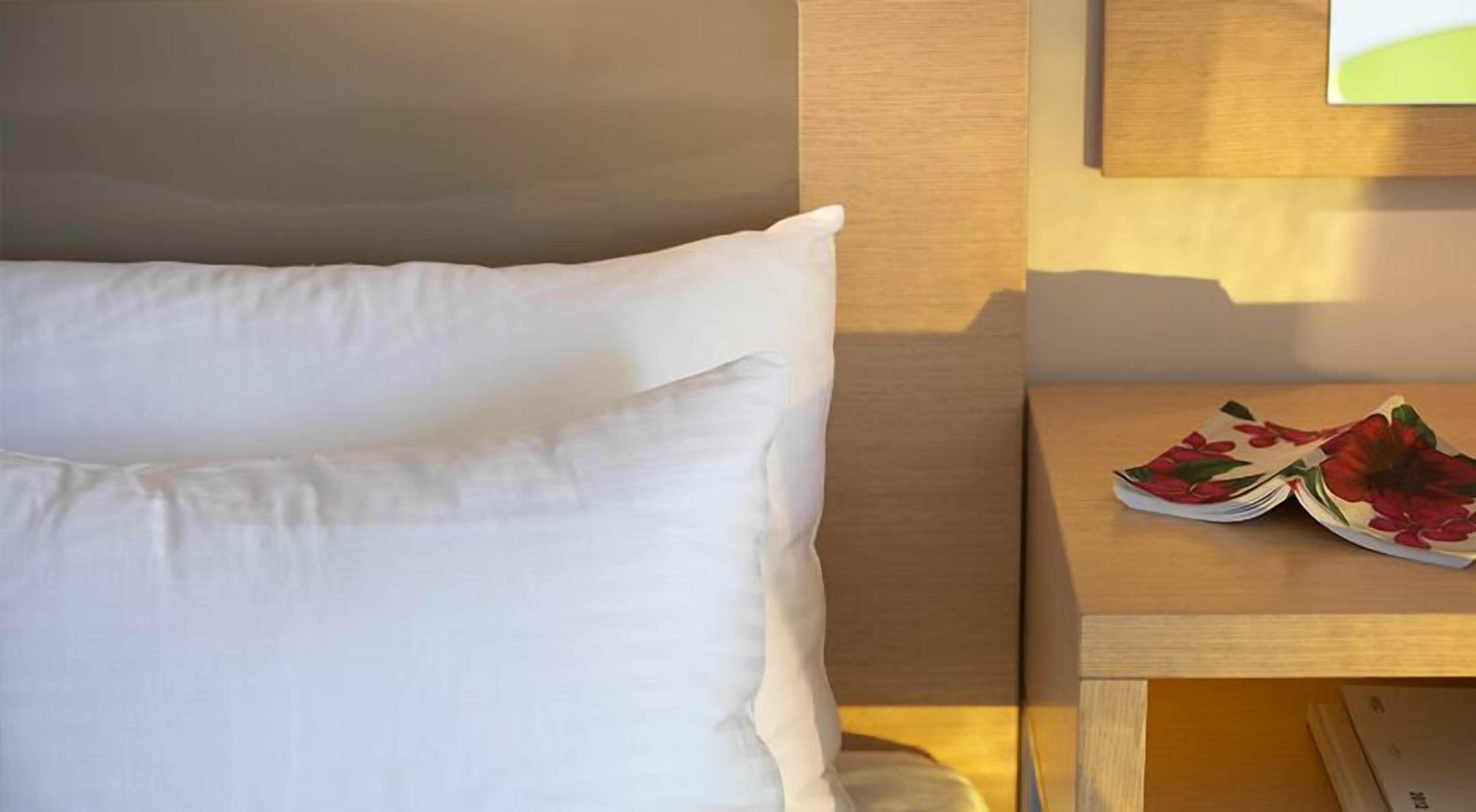 A neatly made bed with white pillows and a wooden nightstand beside it.