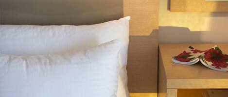 A neatly made bed with white pillows and a wooden nightstand beside it.