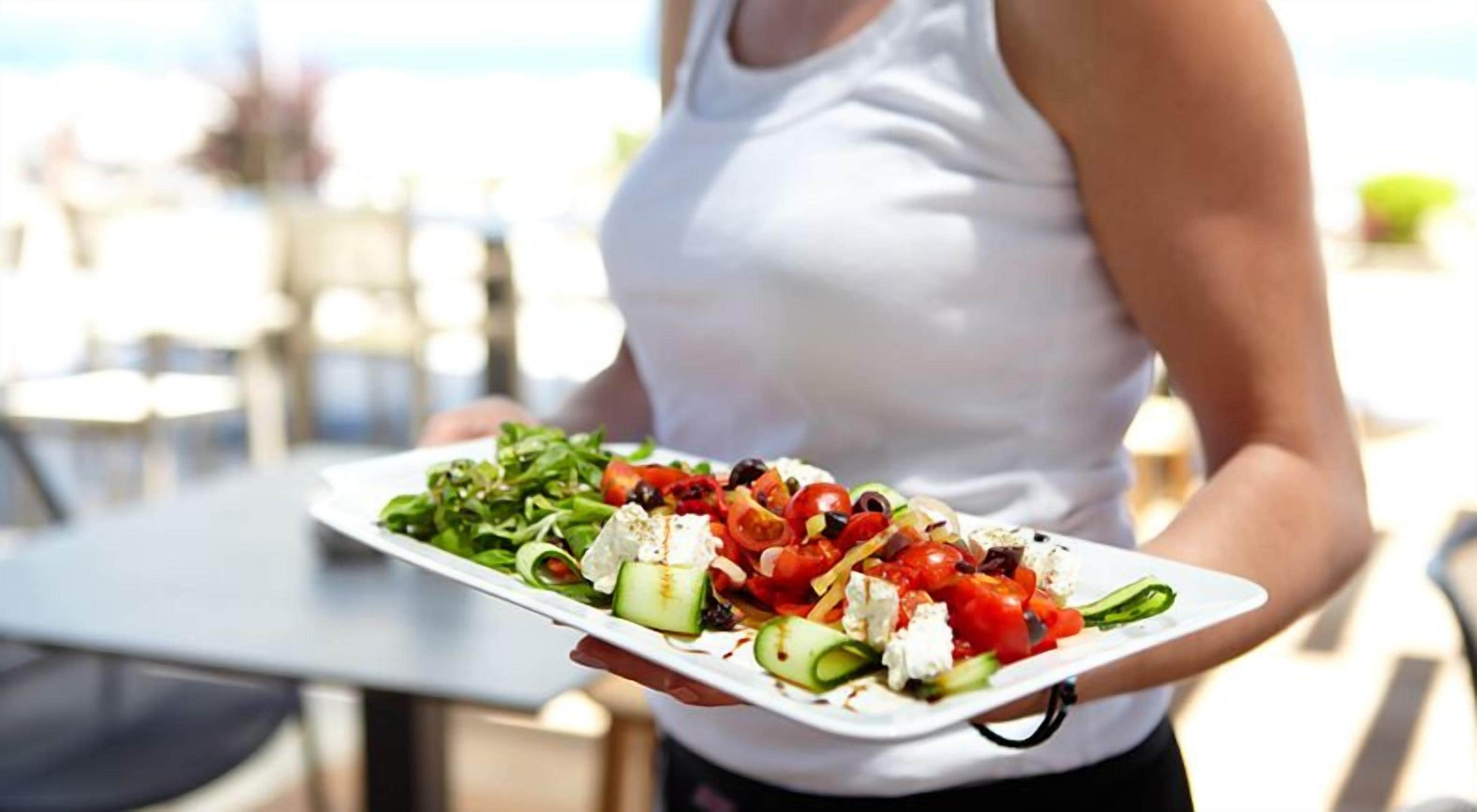 A person holding a plate of salad outdoors.