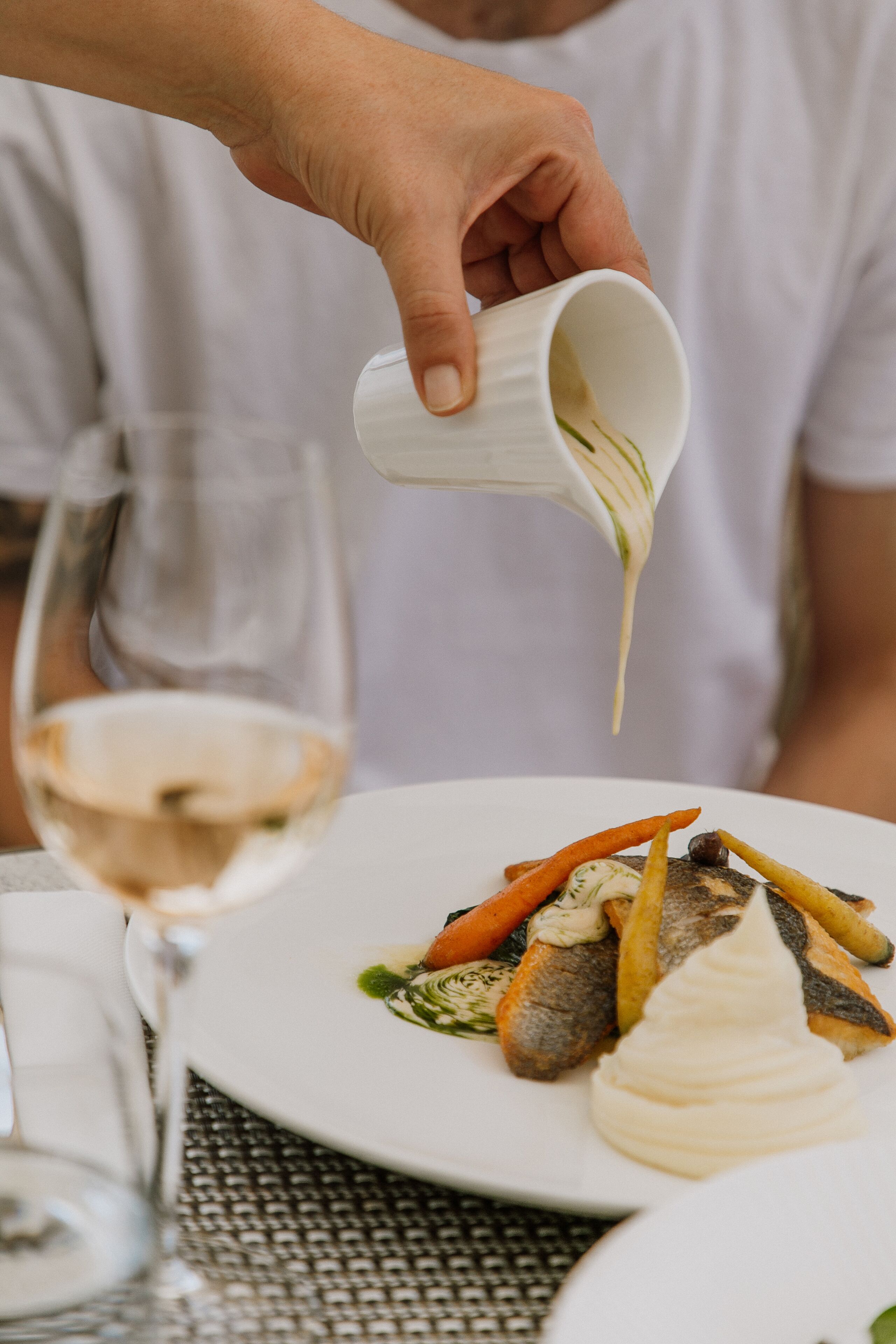 Una persona sirviendo salsa sobre un plato de pescado y verduras.