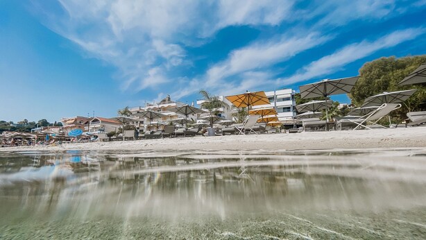 A beachside hotel with clear waters, sun loungers, and umbrellas.