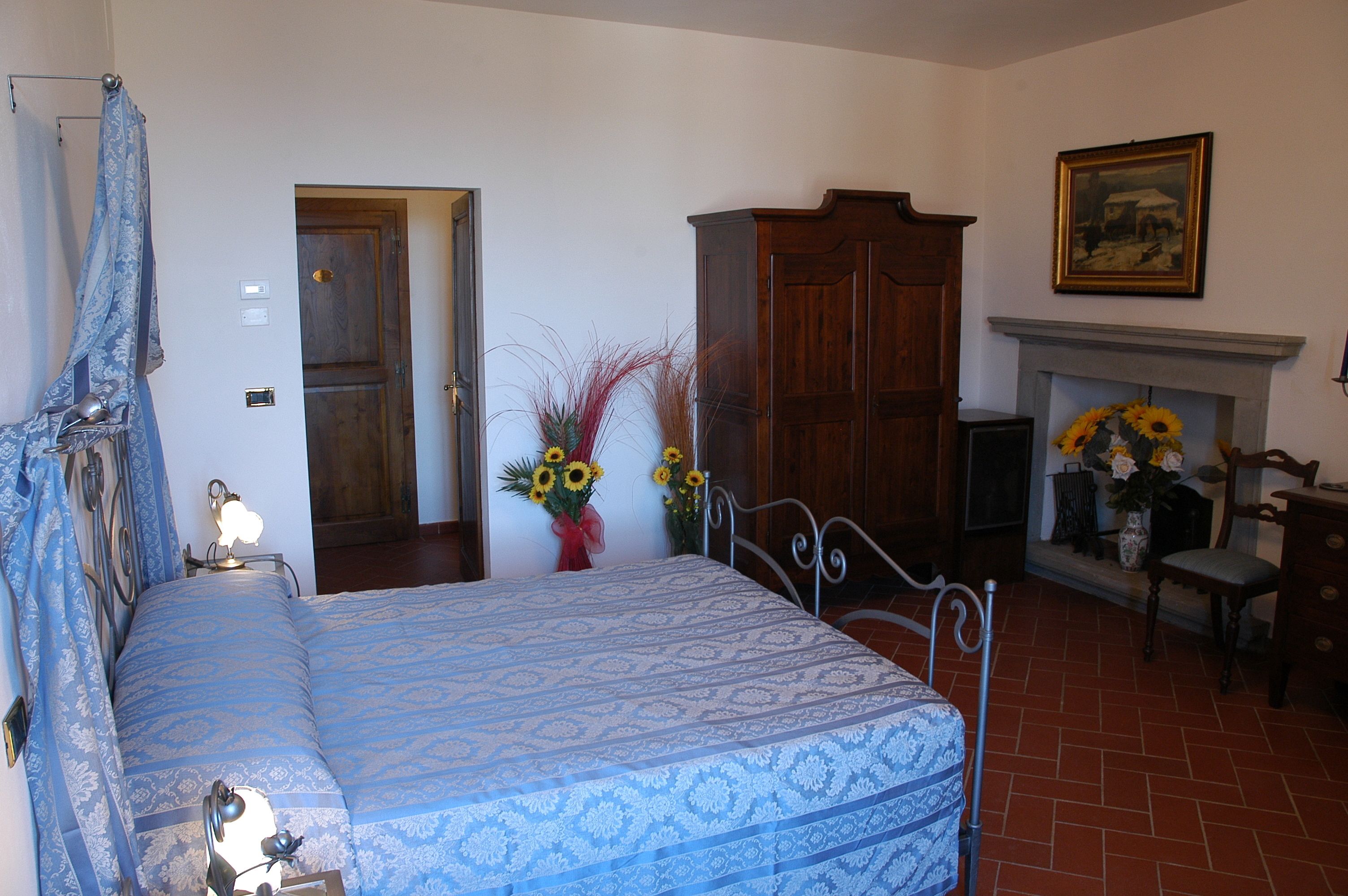 Een slaapkamer met een bed, een houten garderobe, een open haard en een schilderij aan de muur.