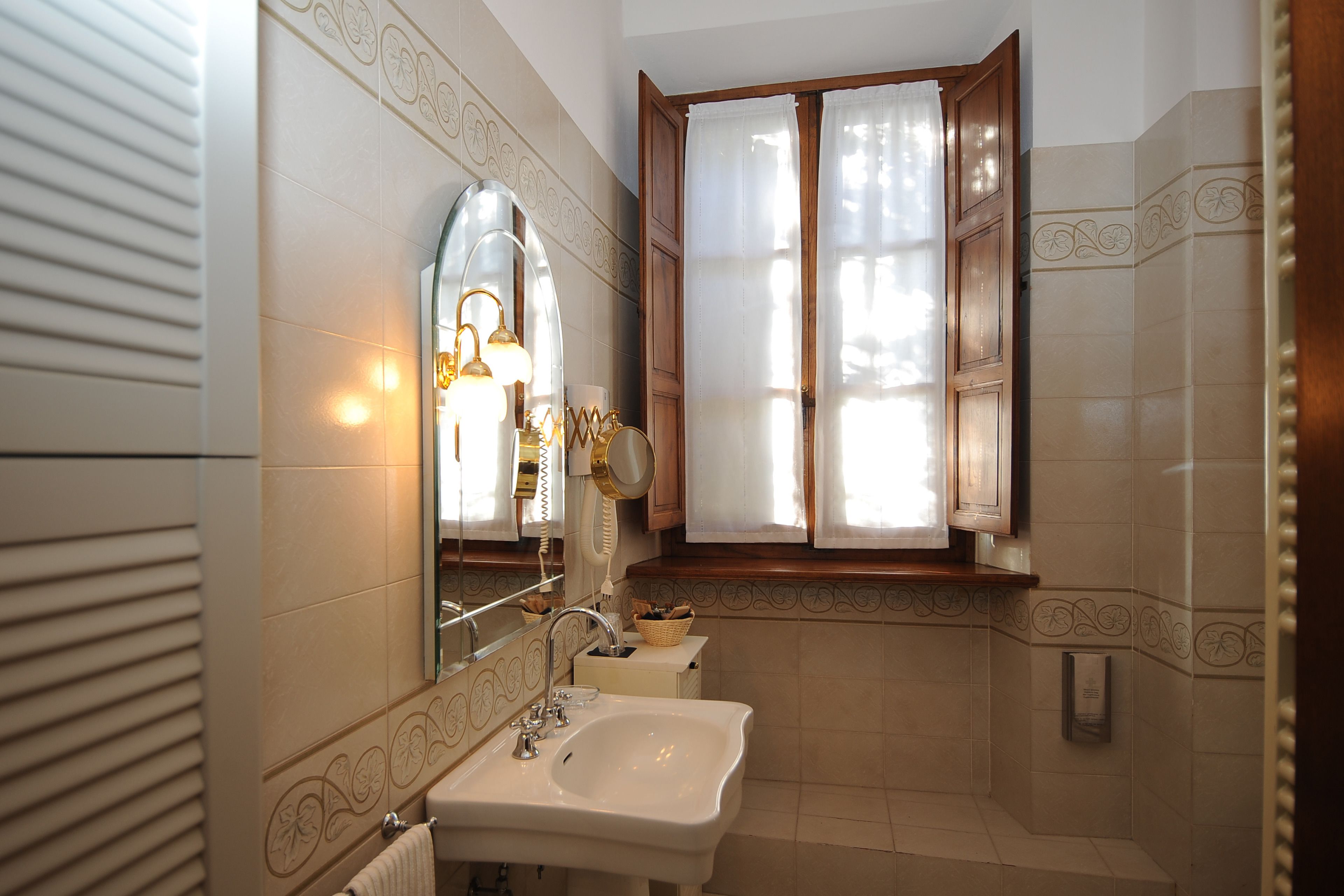 A bathroom with a sink, mirror, and window with curtains.