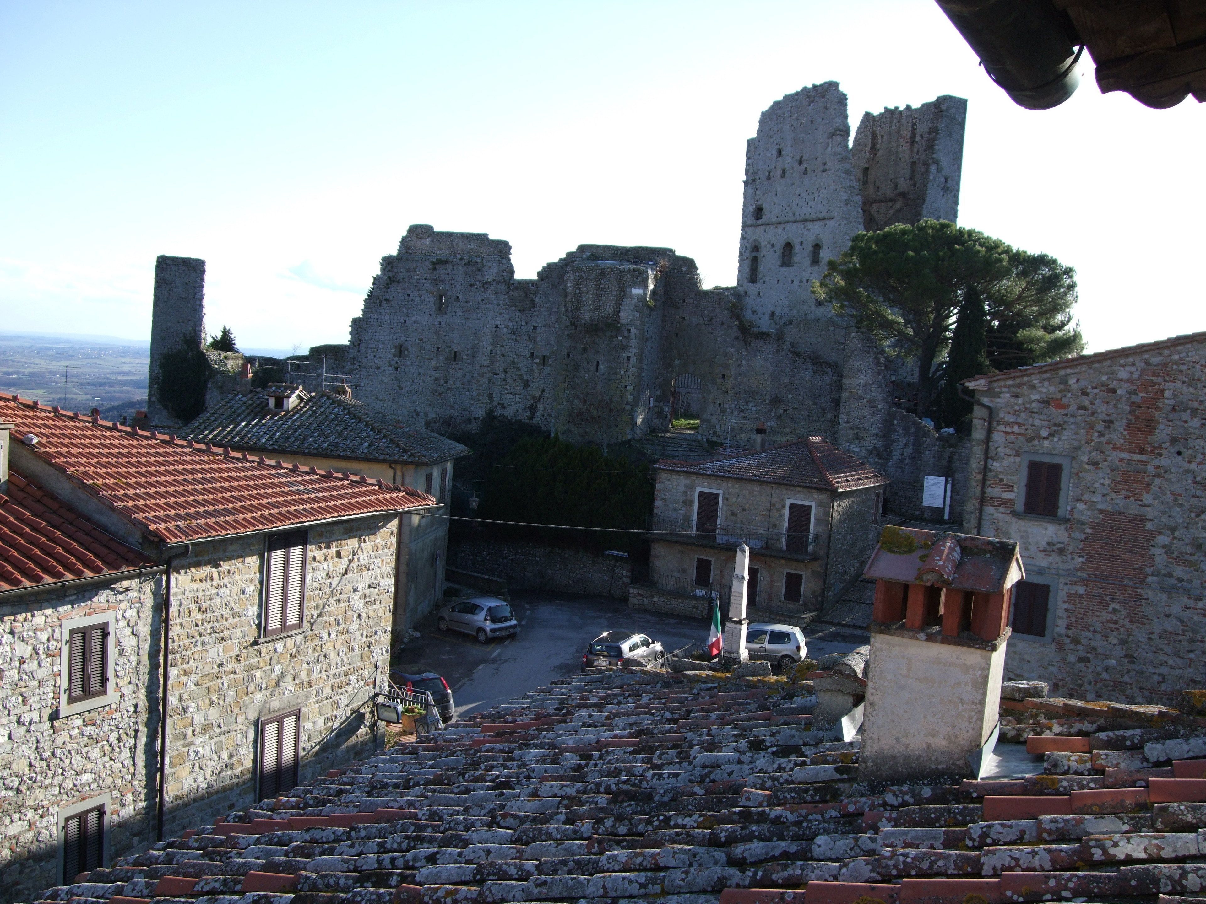 Un edificio histórico de piedra con tejado rojo, un patio con escalones y una vista de una gran fortaleza al fondo.