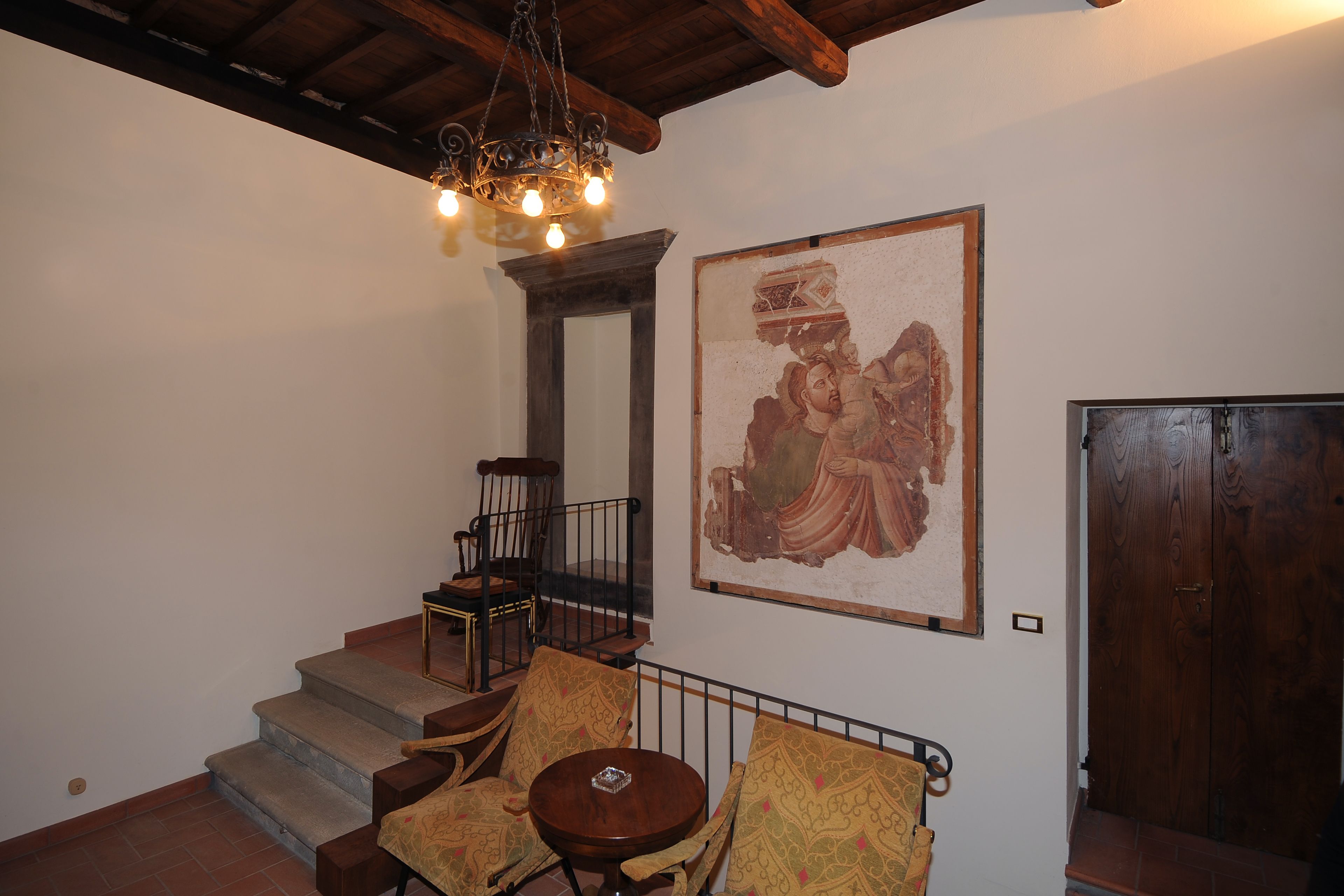 A staircase with a wooden railing, a round table with a decorative cover, and a large framed artwork on the wall.