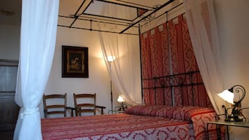 Ein Schlafzimmer mit Himmelbett, Nachttisch mit Lampe, zwei Stühlen und einem gerahmten Bild an der Wand.