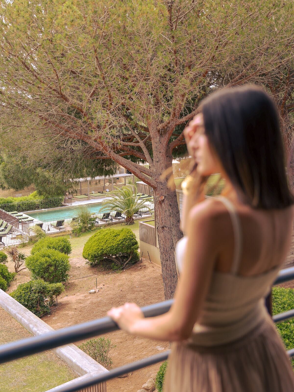 A person overlooking a pool area with a view of a tree and a fenced garden.
