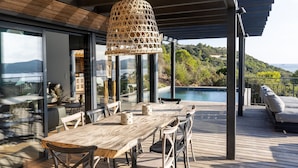 A wooden deck with a table and chairs, overlooking a pool and lush greenery. - Résidence Casarina (Bonifacio)