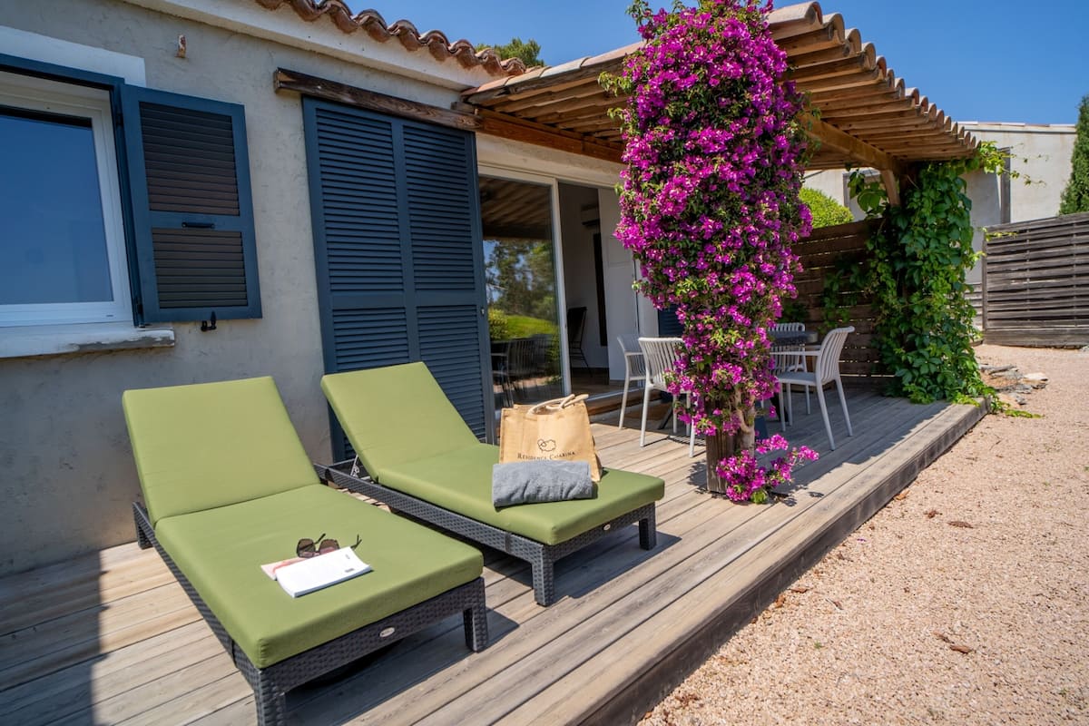 A covered outdoor area with two green lounge chairs, a wooden table, and a hanging flower arrangement.
