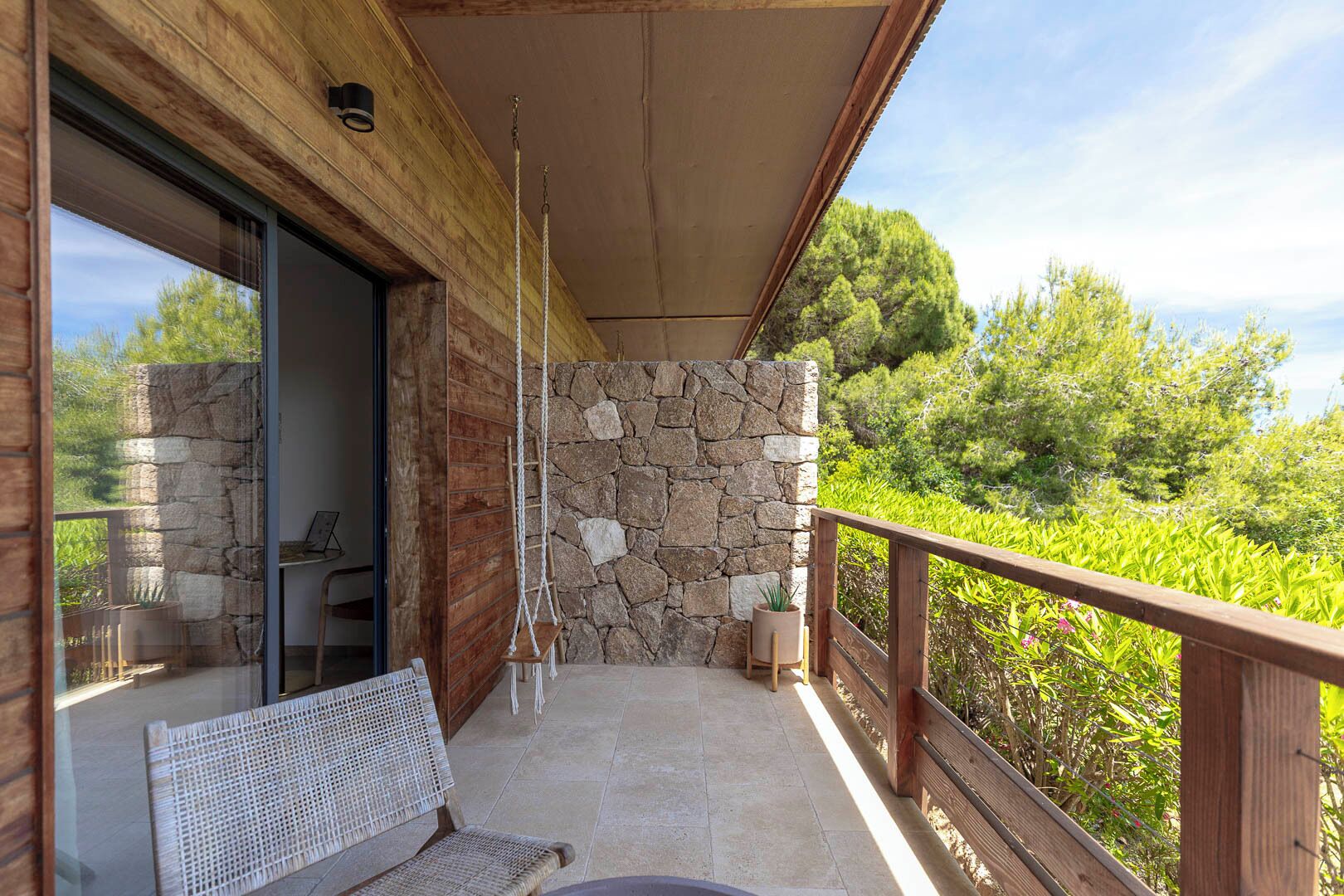 Un balcon doté d’un mur en pierre, d’une balustrade en bois et offrant une vue sur la verdure.